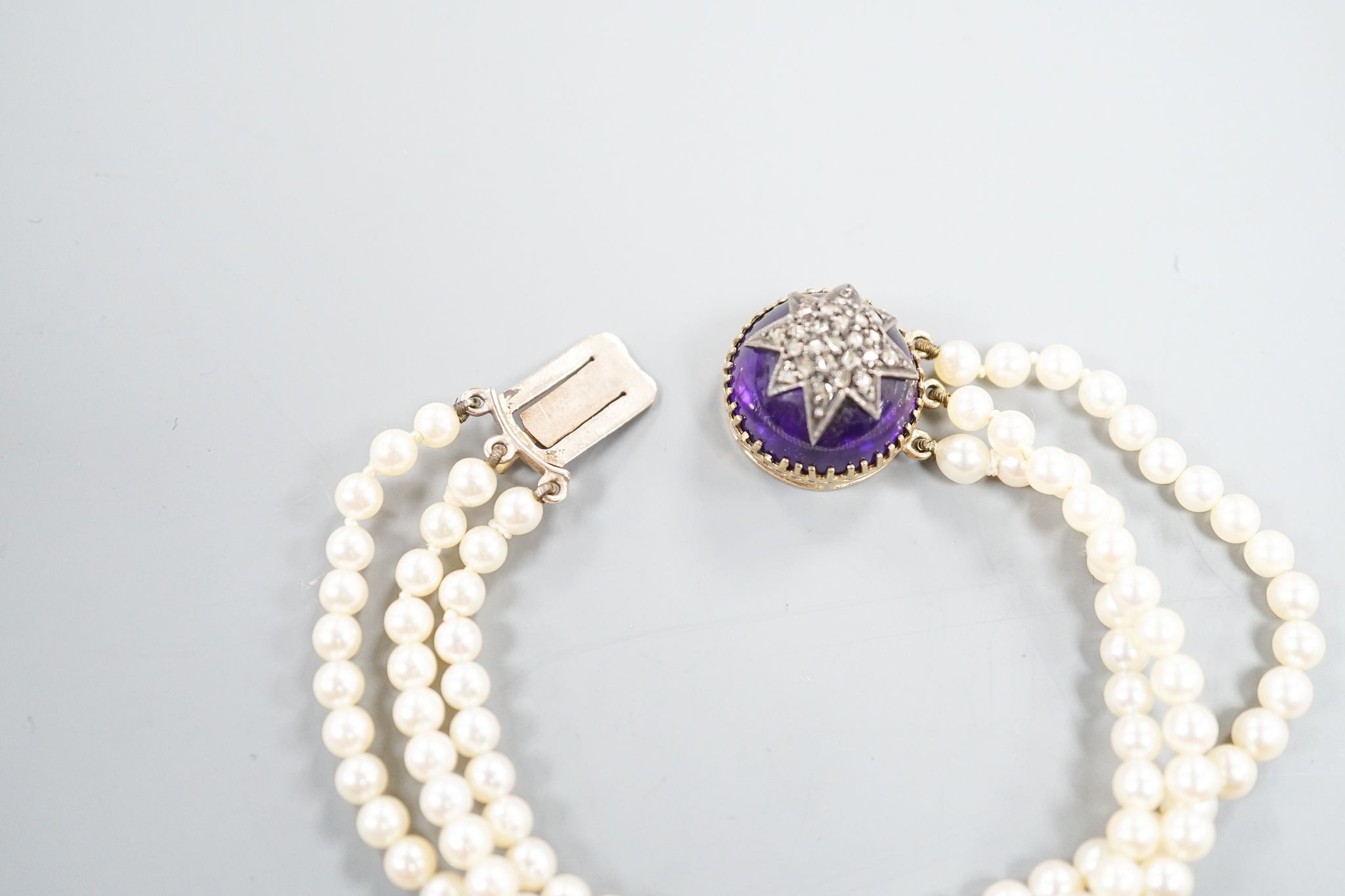 An early 20th century triple strand cultured? pearl bracelet, with rose cut diamond and cabochon amethyst set yellow metal clasp, 17.5cm, gross weight 21 grams.